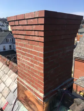 A red brick chimney with stepped courses, photographed from a neighboring roof.