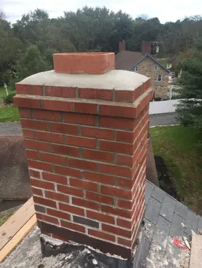 A rebuilt red brick chimney with a concrete crown on a shingle roof.